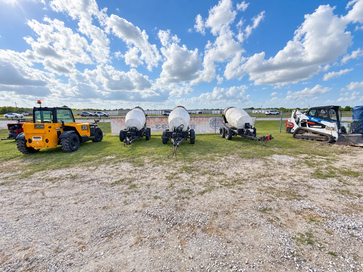 Three towable concrete mixers lined up at the yard between a telehandler and a skid steer.