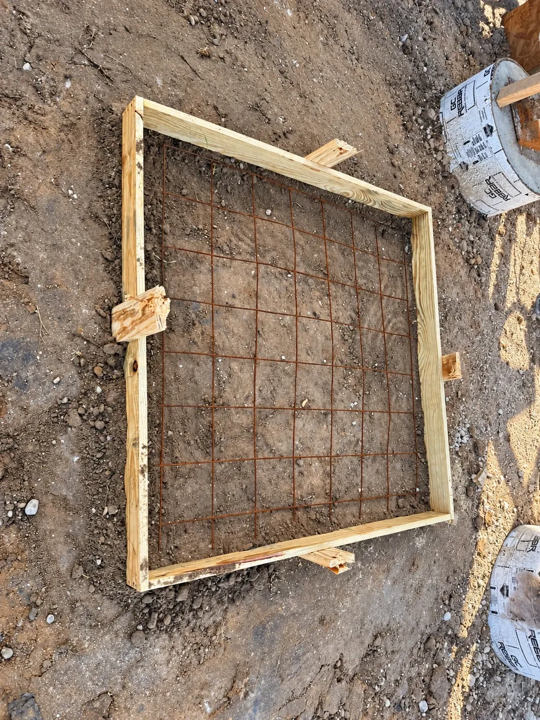 A square timber form with rebar mesh set on graded ground.