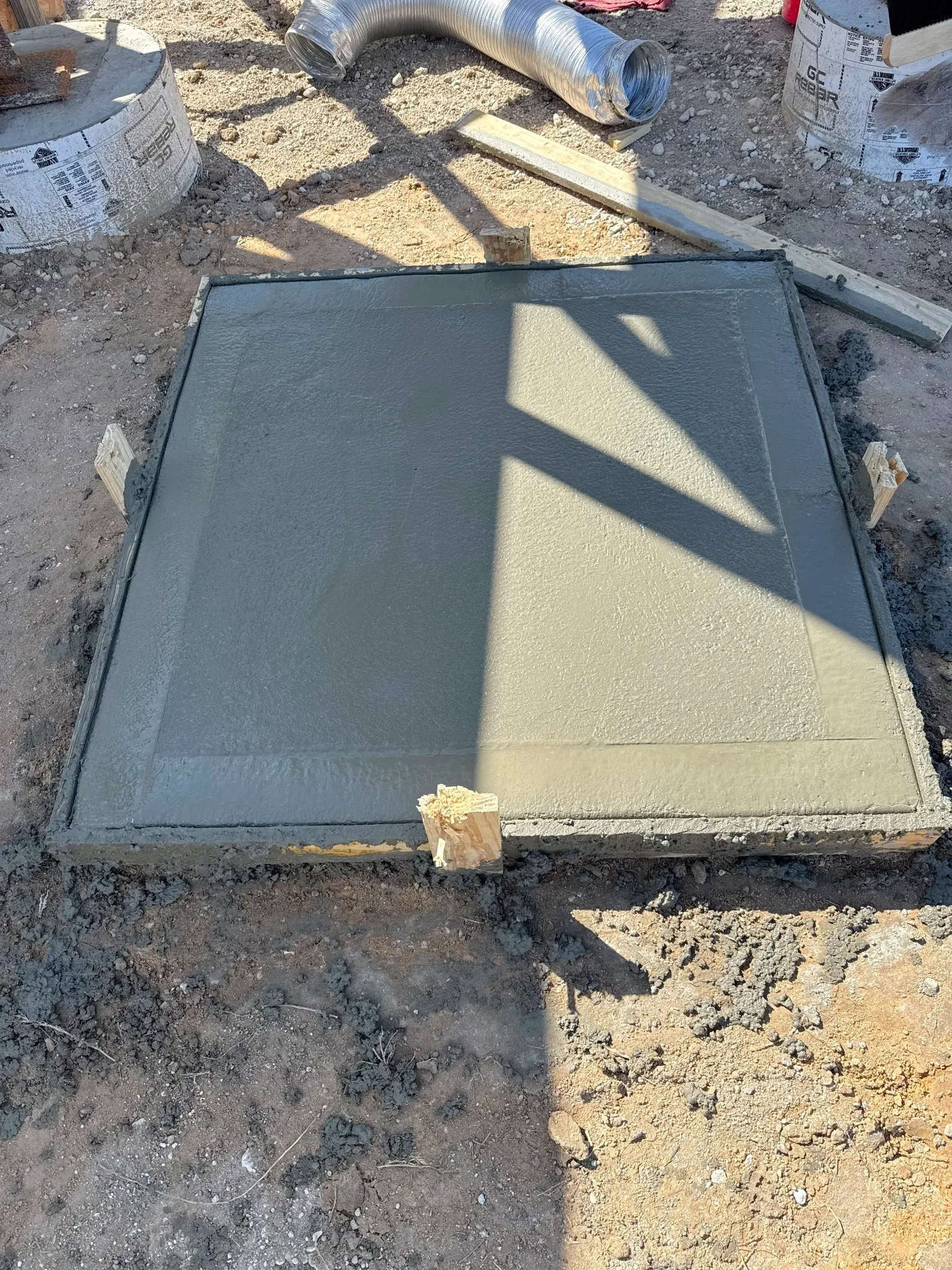 A freshly poured square concrete pad in its form on a jobsite.