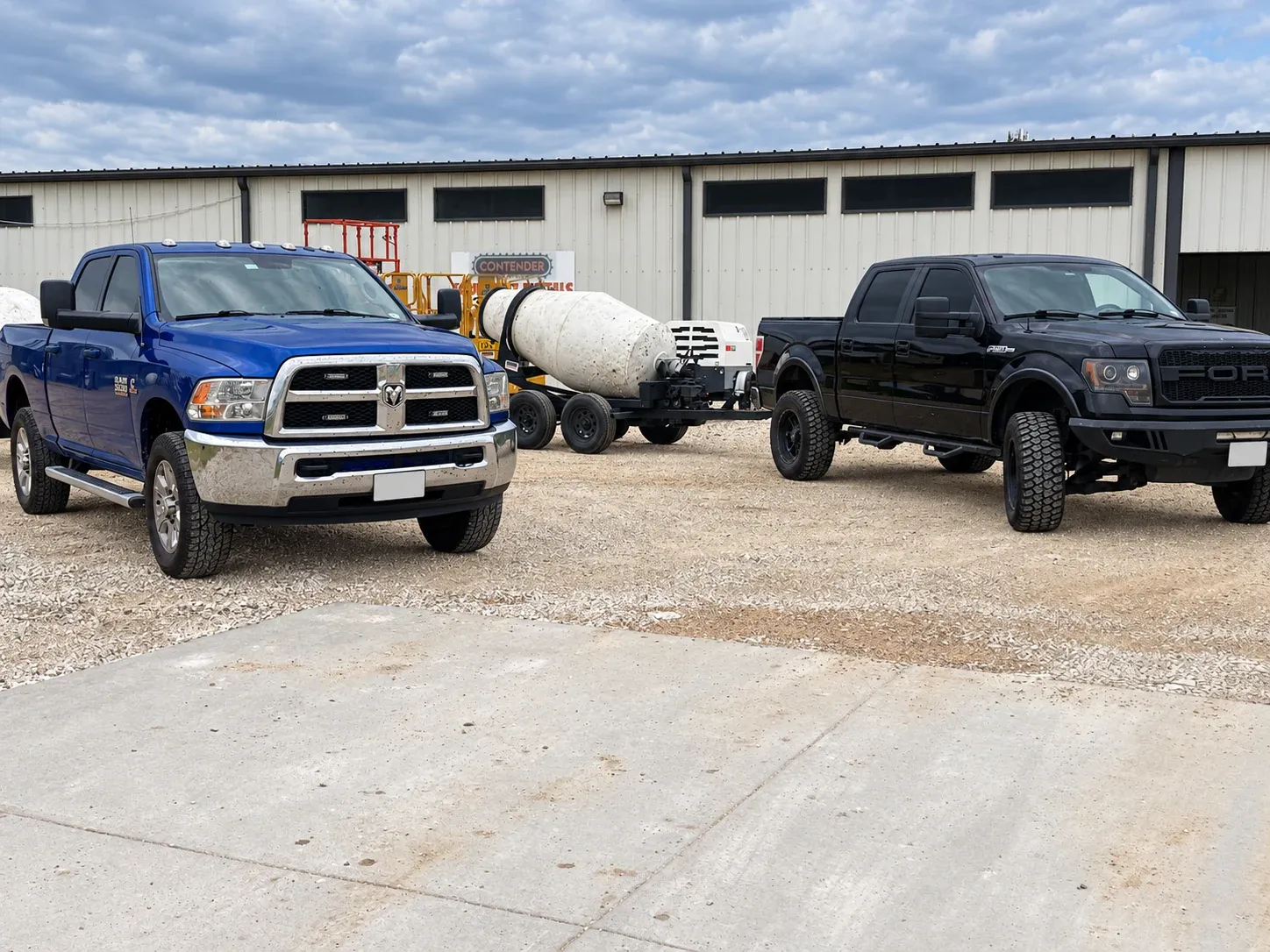 Two pickups and a towable mixer parked outside the yard building.