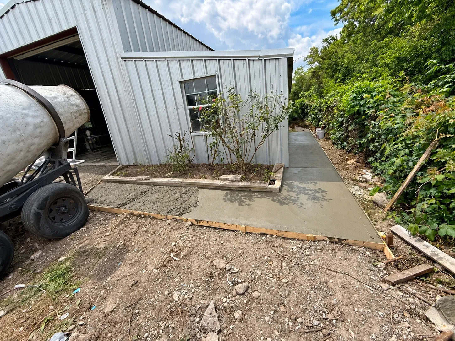 A fresh concrete walkway poured beside a metal building, the mixer still alongside.