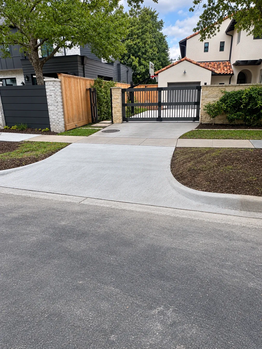 A new concrete driveway apron curving from the street up to a black gate.
