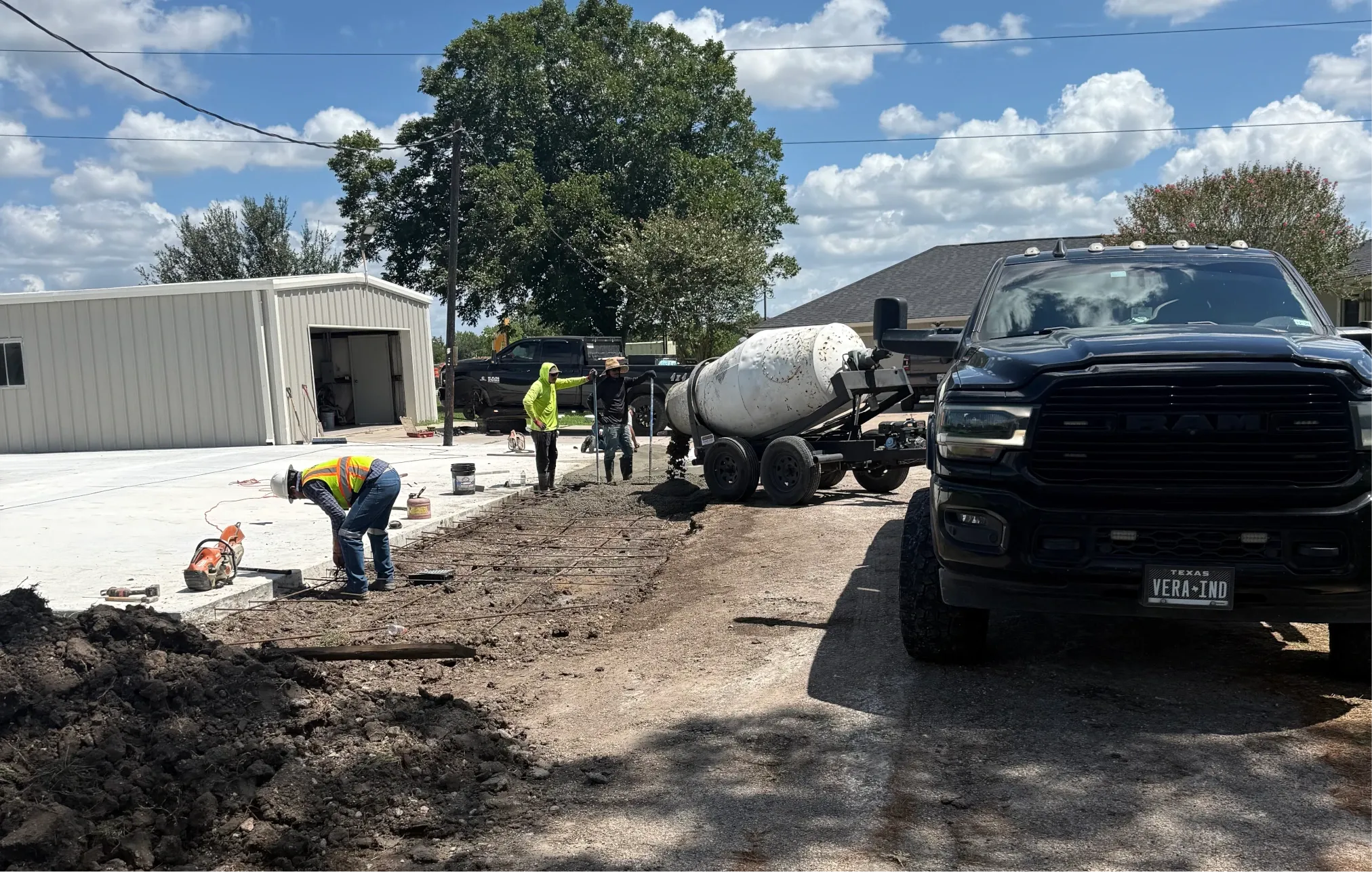 A crew placing rebar on a fresh slab beside a small-batch mixer trailer.
