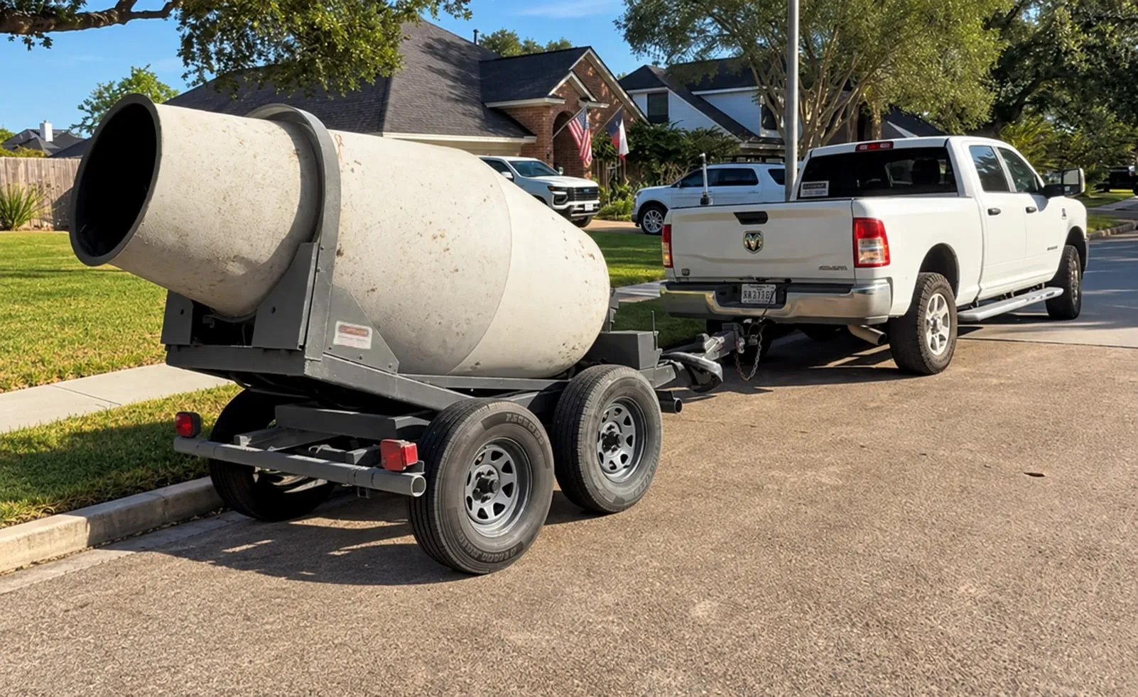 A white pickup truck with a concrete mixer trailer hitched behind it on a home street.