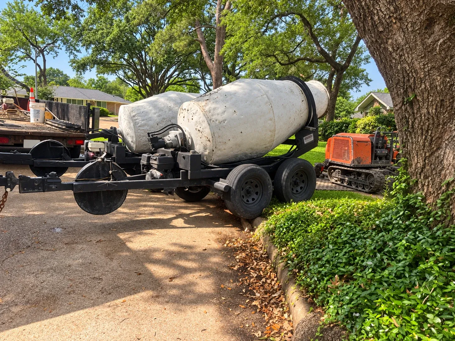 Mixers on a trailer set close to a house, under a tree, with a tracked buggy beside them.