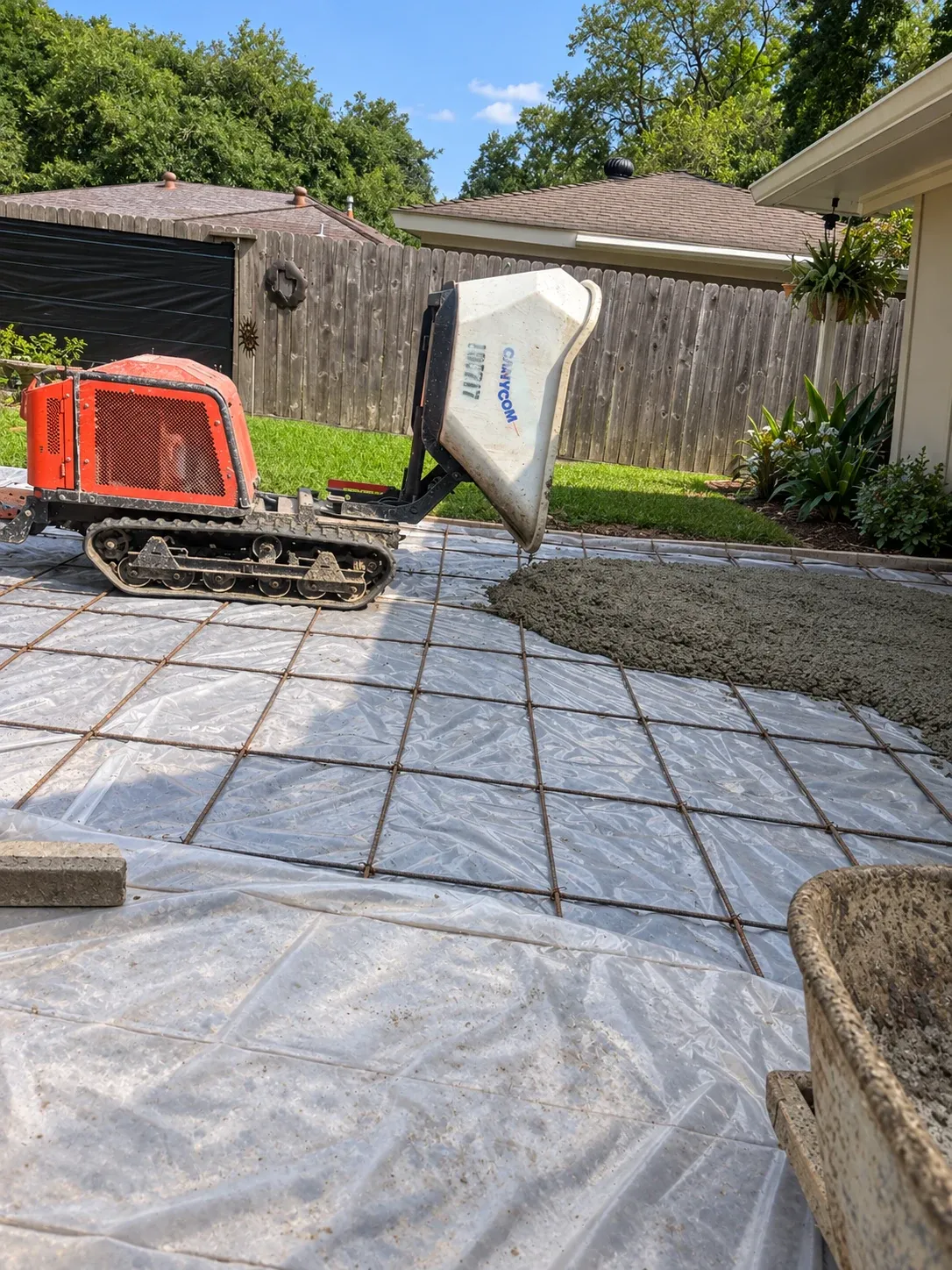 A tracked buggy tipping concrete onto plastic sheeting and rebar mesh for a slab.